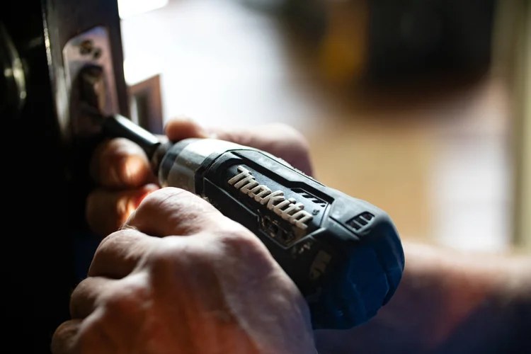 Hands using a cordless drill driver on a door lock